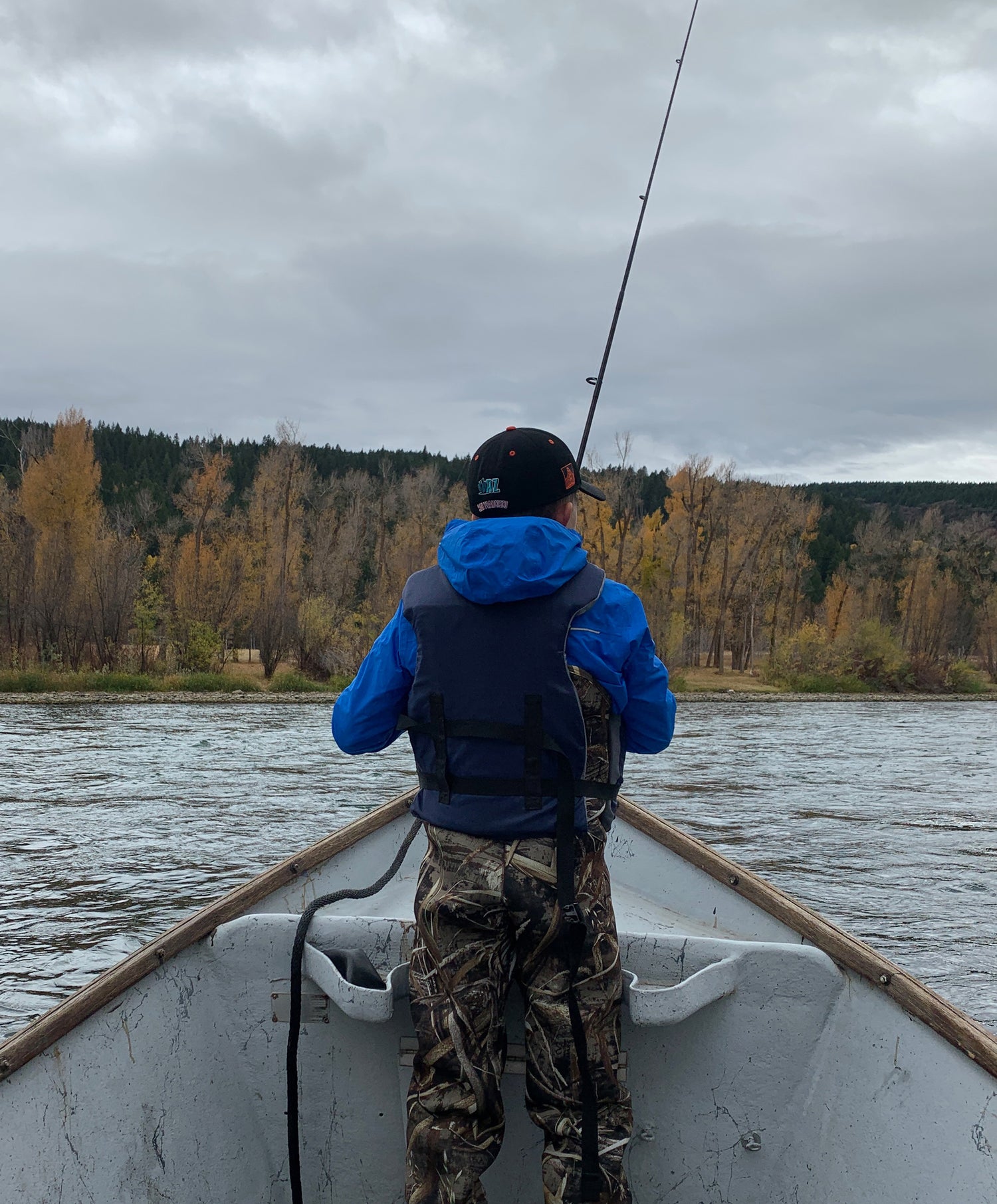 Child fishing from a boat on a lake with trees and cloudy sky in the background