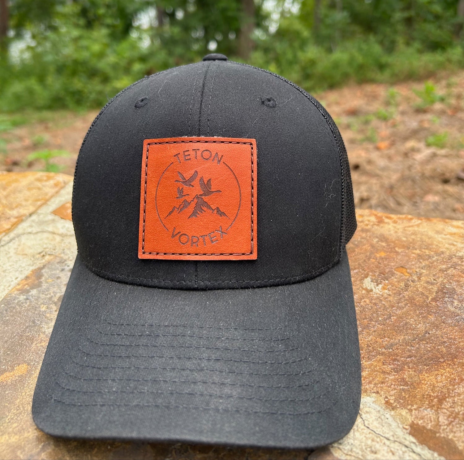 Black cap with a Teton Vortex patch on a wooden surface with a forest background